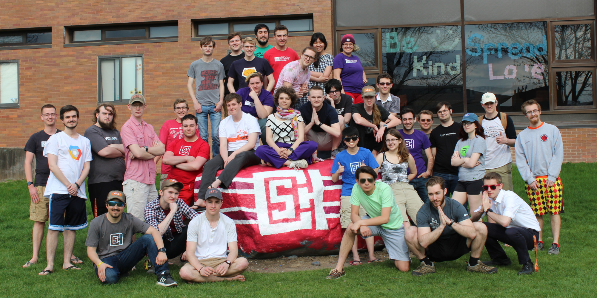 CSHers crowd around a rock painted red with a CSH logo on it in white