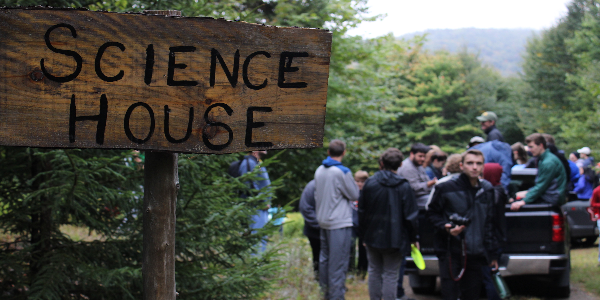 A sign that reads Science House with CSHers in the background. Taken at Fall Camping 2019